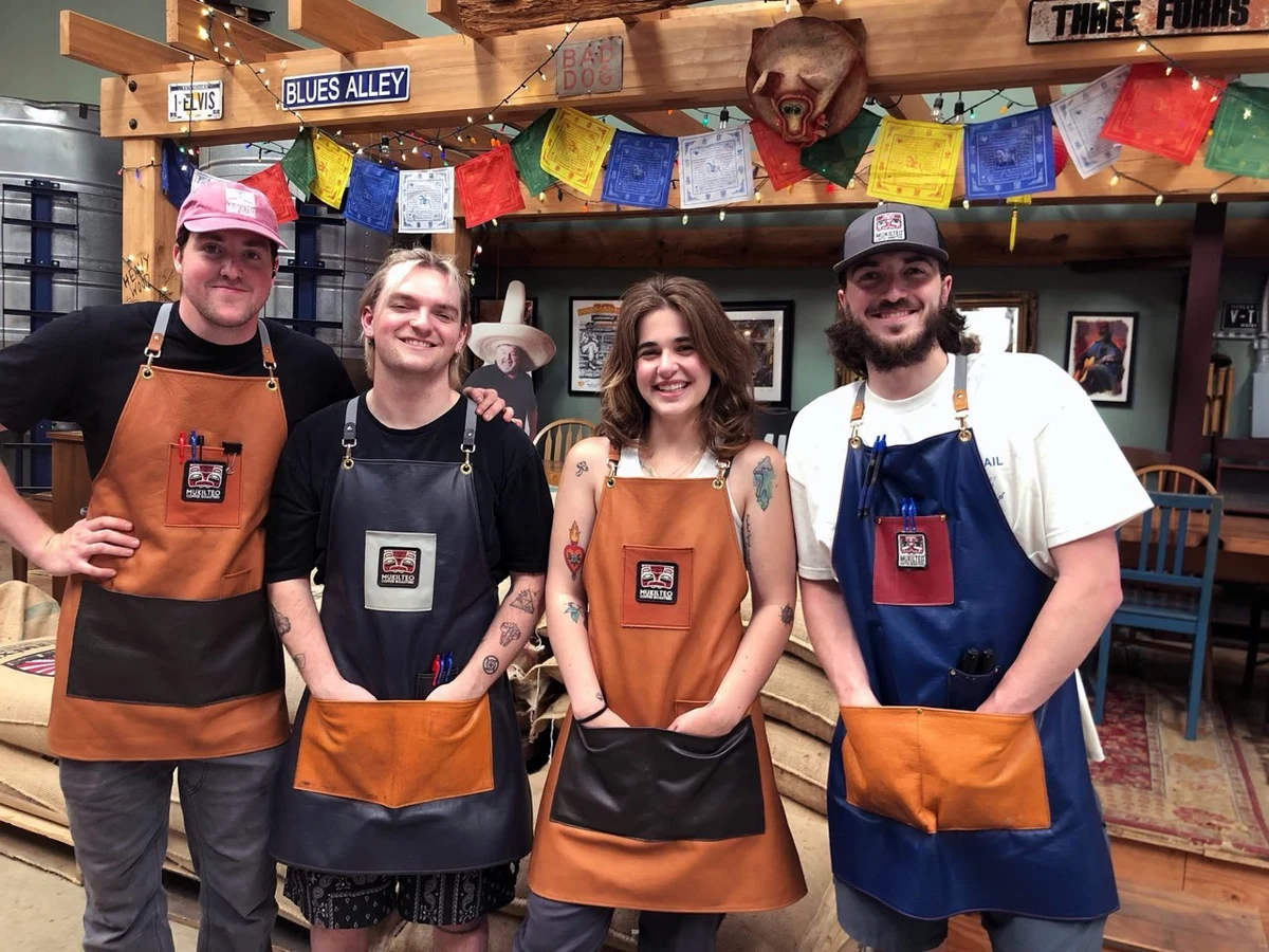 Four customers wearing leather aprons with contrasting pockets and coffee company patches