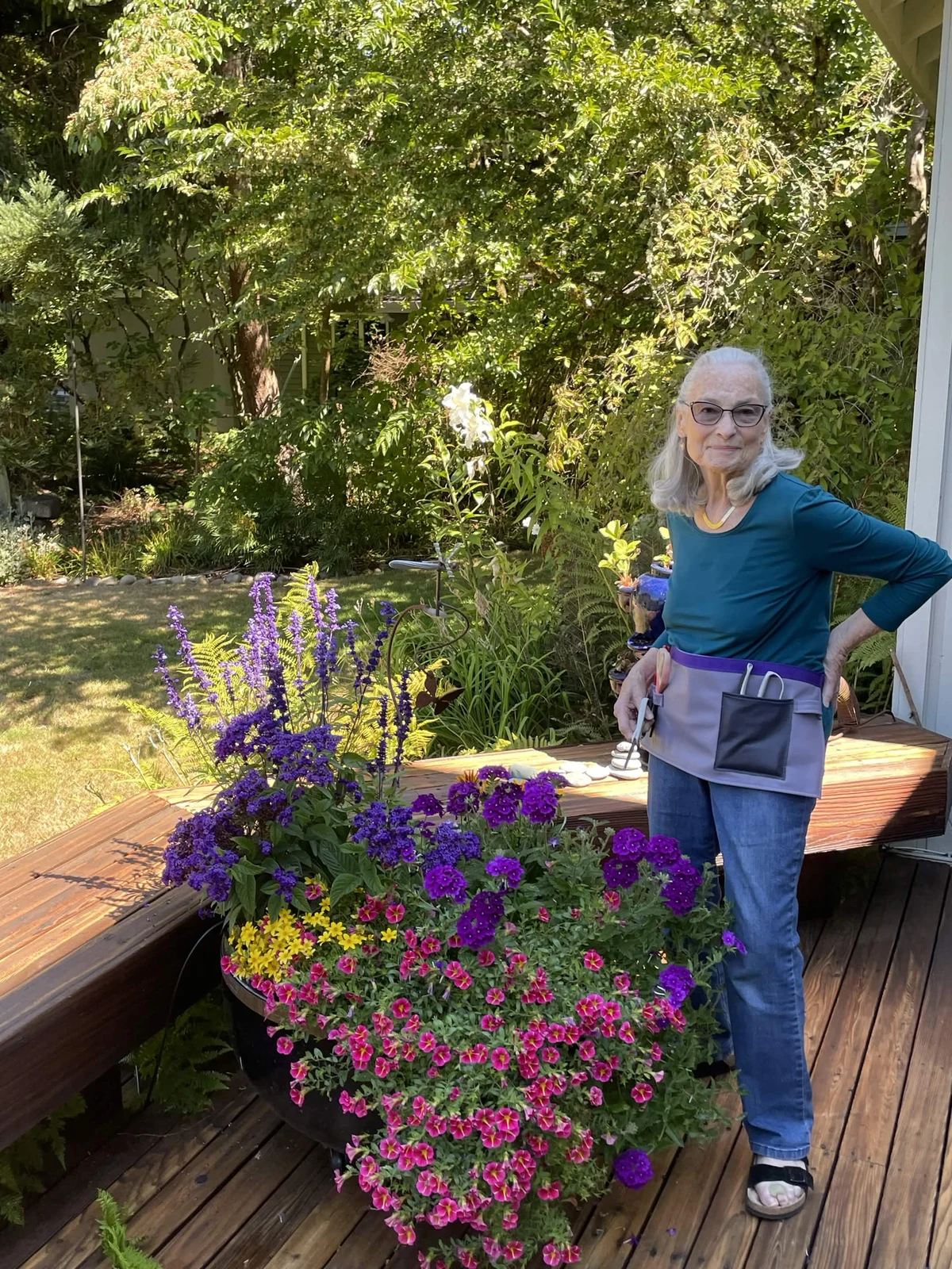 Customer wearing a lavender half apron beside flowering planters in a garden