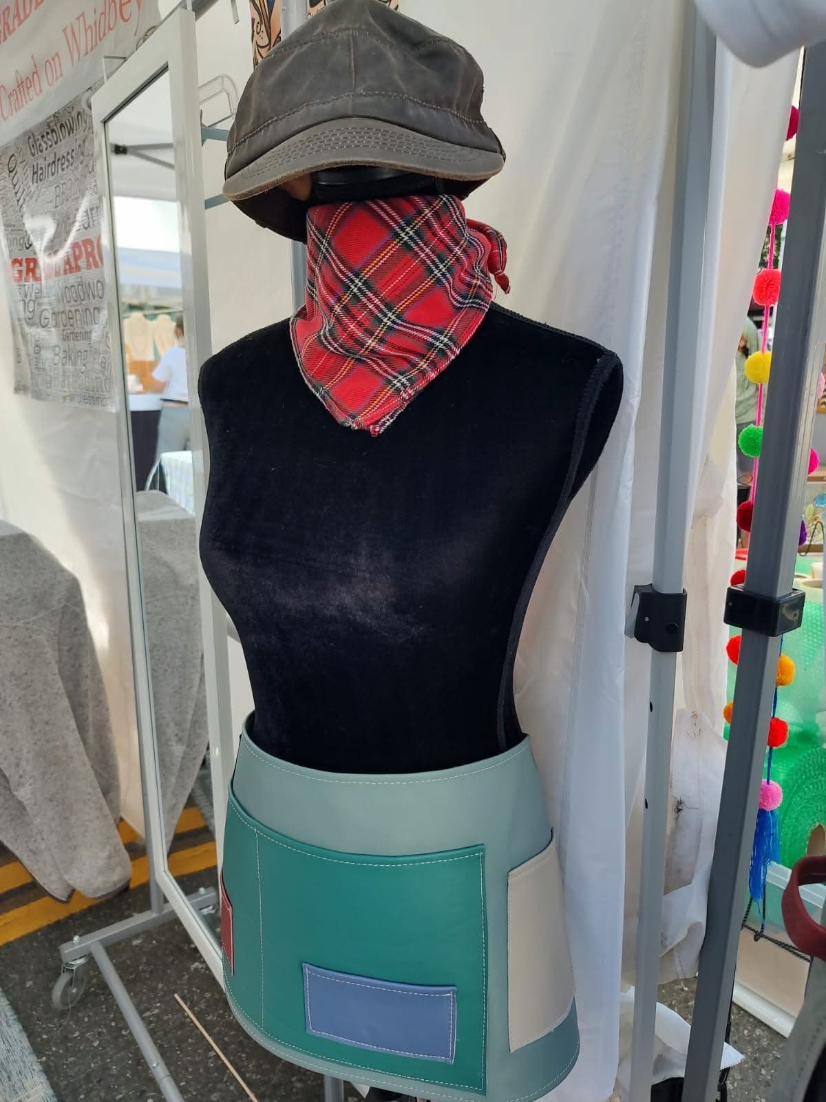 A teal leather half apron displayed on a mannequin at the festival booth.