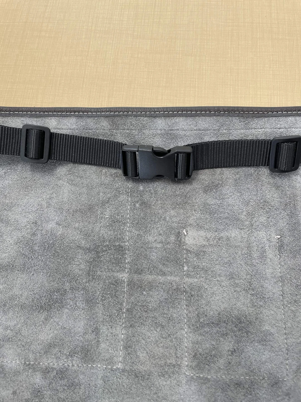 Black side-release buckle and adjustable woven belt across the gray reverse of a leather apron
