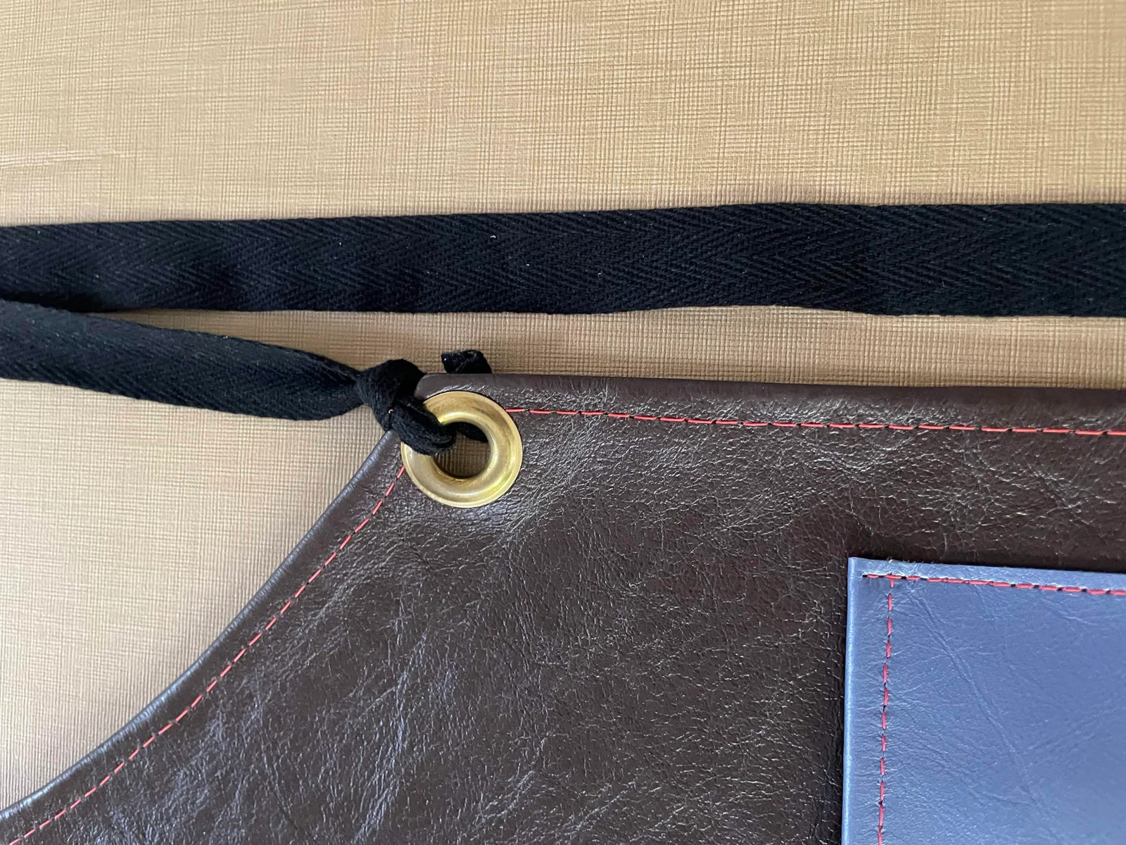 Leather grain, red stitching, and a woven tie through a gold-tone eyelet