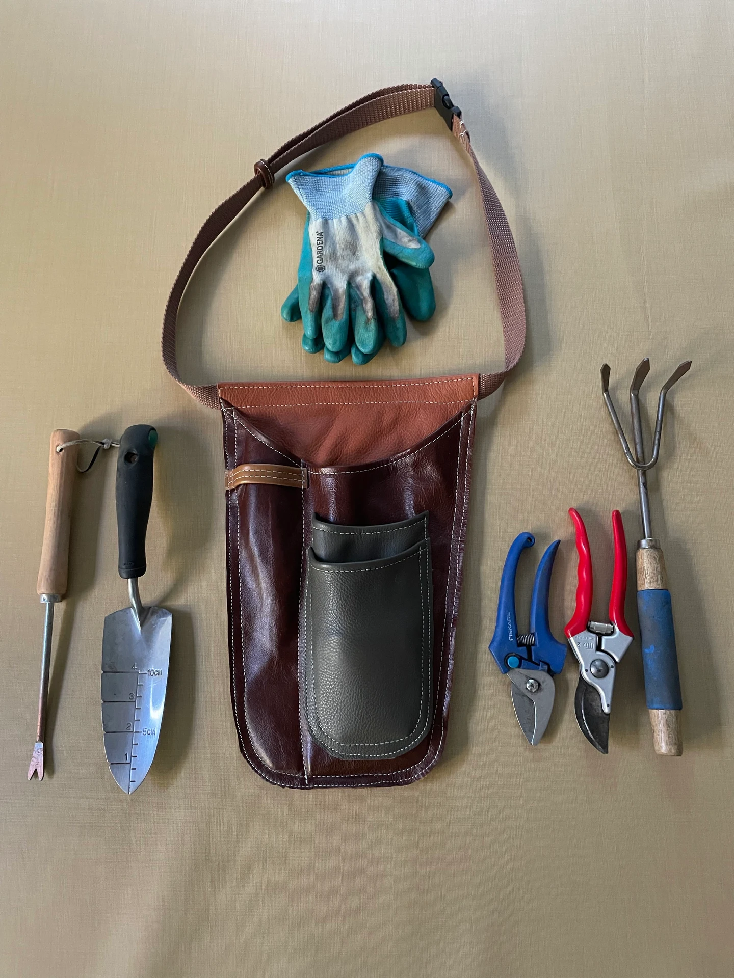Garden tool holster prototype laid out beside gloves, a trowel, pruning shears, and a cultivator