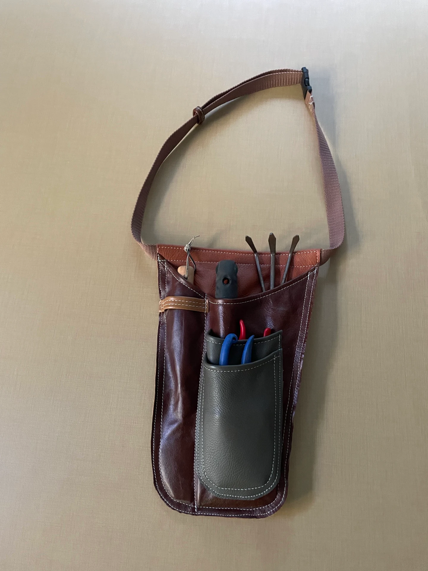 Burgundy leather garden holster prototype with hand tools in its main pocket and pruning shears in the front pockets